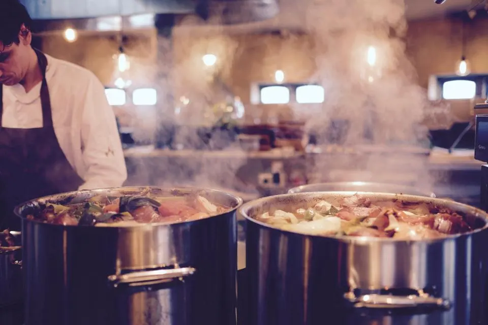 Steam rising from stock pots under a kitchen hood